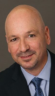 A bald man with a shaved head wearing a suit.